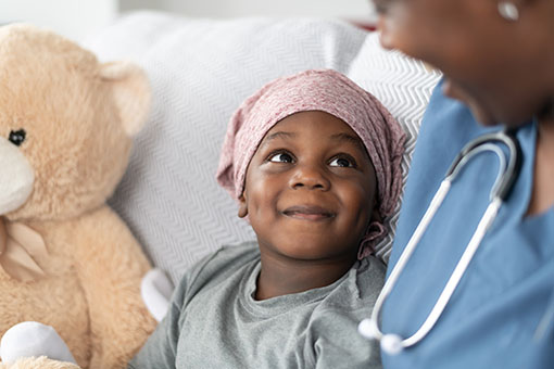 Smiling boy with cancer comforted by female doctor