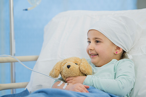 Girl with cancer holding teddy in hospital