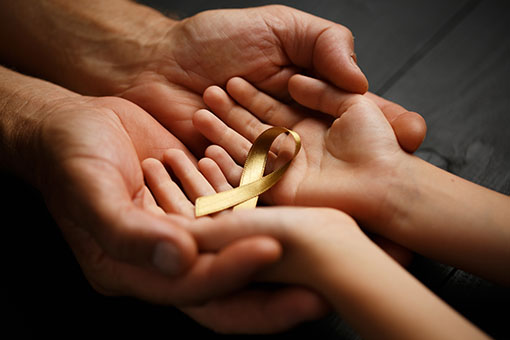 golden ribbon childhood symbol of the fight against cancer in children in hands